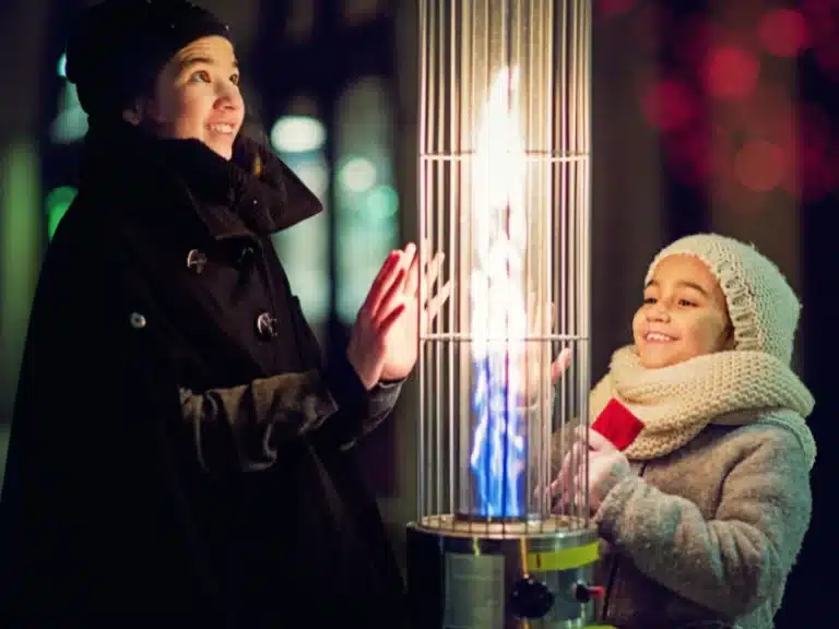 mother and daughter warming their hands on a vertical outdoor heater