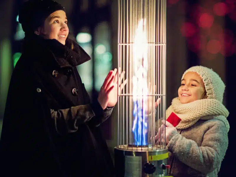 mother and daughter warming their hands on a vertical outdoor heater