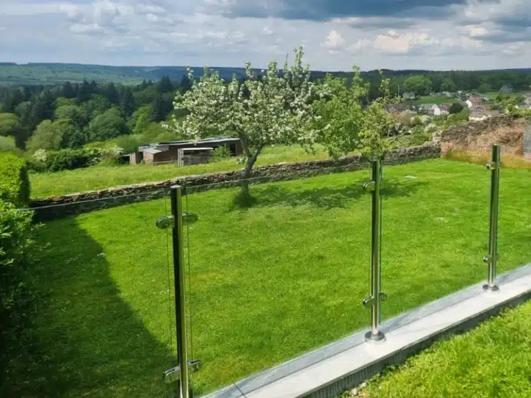 two areas of green garden at the top of a hill overlooking a village separated by glass balustrades