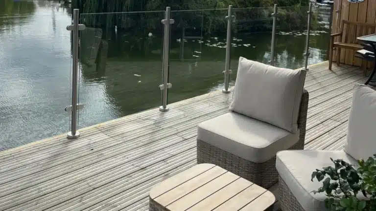 minimalistic thatched wood garden furniture on a wooden plank deck with a metal framed glass balustrade next to a flowing river