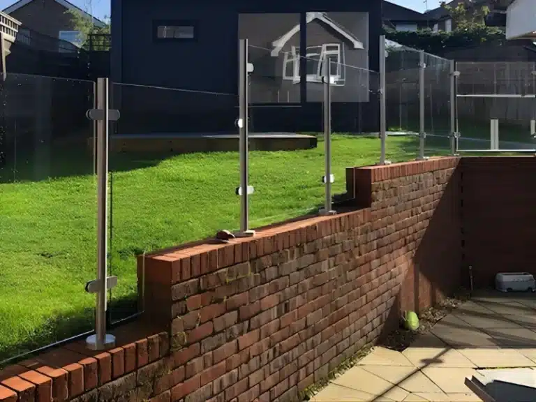 high brick wall with a glass balustrade railing separating a patio and a small grass hill
