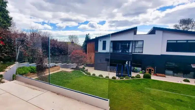 curving stone slab stair case with a frameless glass balustrade railing leading down past a freshly cut garden towards a large modern house with children's toys outside