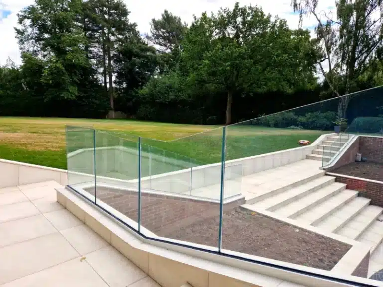 Large pale block stair case with frameless balustrade next to a freshly cut grass field
