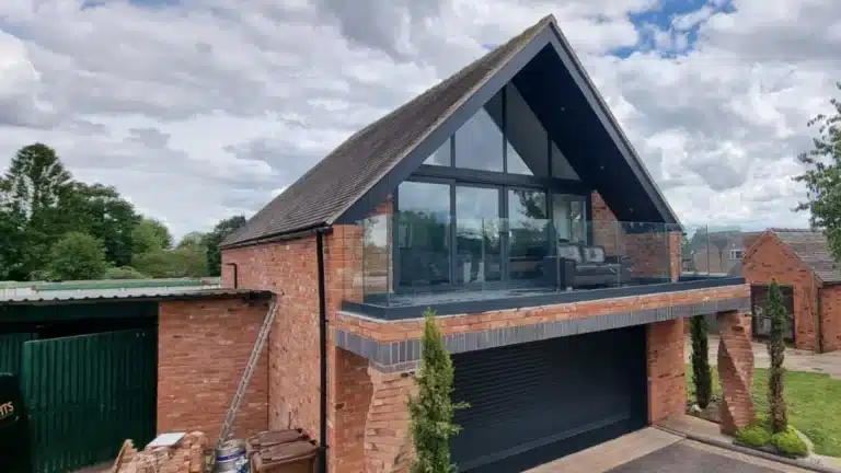 red brick house with a large enclosed balcony fenced in by a frameless glass balustrade overlooking a driveway