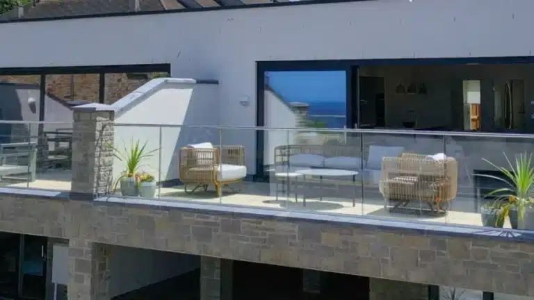 Raised stone patio with a glass balustrade railing and thatched wood furniture and a glass central table