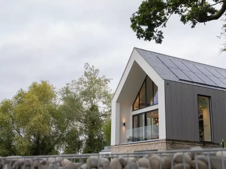 large grey house with large windows and a balcony contained by a frameless glass balustrade