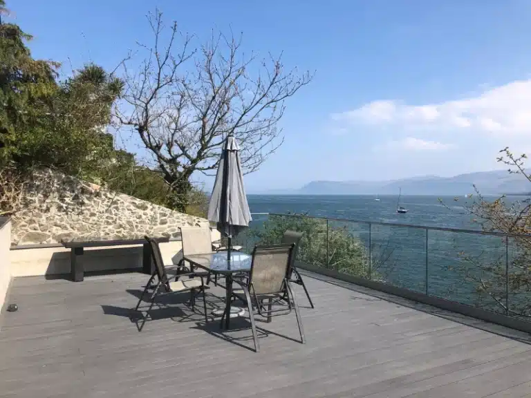 clean wooden deck with a black table and chair outdoor furniture set overlooking the sea and boats sailing by