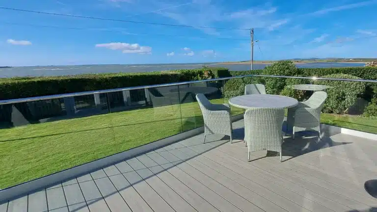 grey wood patio with a glass balustrade railing and wicker garden furniture looking out to the sea