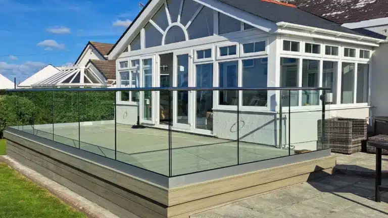 Raised wooden patio outside a glass conservatory overlooking a garden with well trimmed hedges