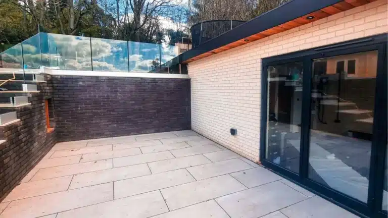 Open grey patio outside a house with stairs and a frameless glass balustrade railing