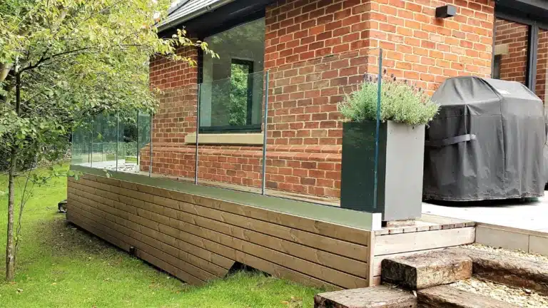 small red brick house with frameless glass balustrade railing next to a small curving garden