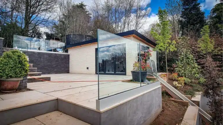 large multi level patio garden with frameless glass balustrades and a treehouse and trampoline in the distance