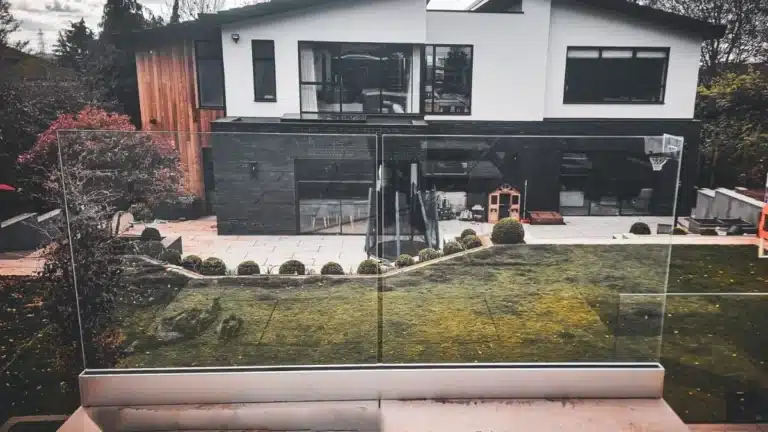 Simple frameless glass balustrade in front of a descending garden leading to a large modern home