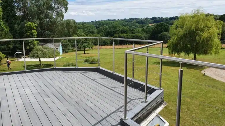 Grey wood-like deck with a metal wire balustrade overlooking a large grass plain with a tall tree
