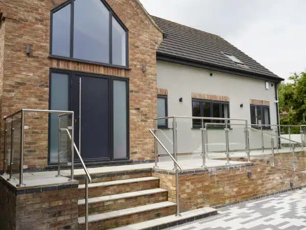 Large modern home with brick patio and glass balustrade railing lining a stair case and ramp