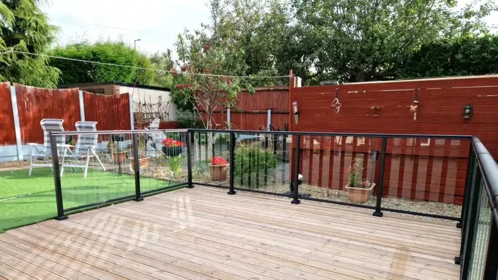 glass slat balustrade with a black frame on a wooden deck in a well decorated garden