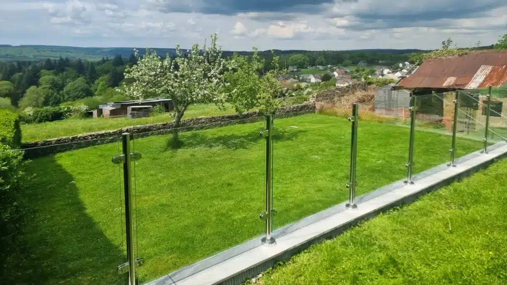 two areas of green garden at the top of a hill overlooking a village separated by glass balustrades