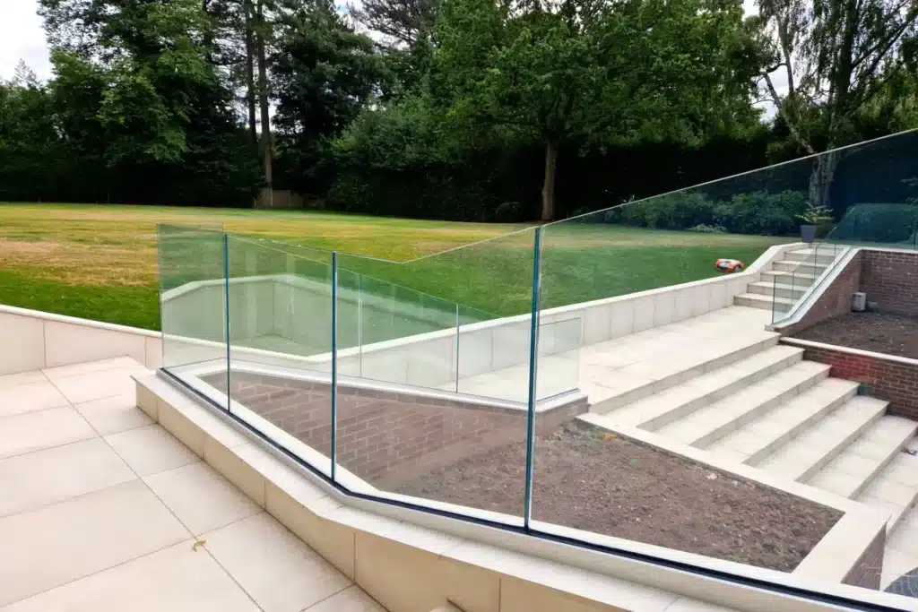 Large pale block stair case with frameless balustrade next to a freshly cut grass field