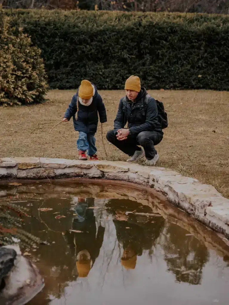 Father and child standing next to a pond looking into the water